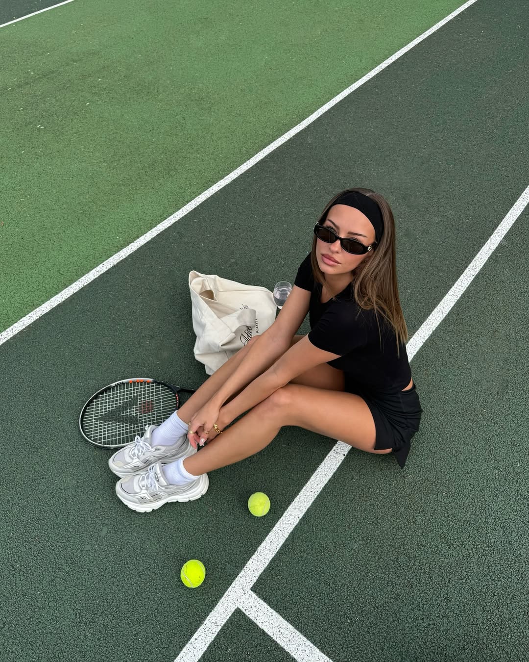 Foto de uma mulher morena usando um look composto por camiseta, short saia, t&ecirc;nis esportivo, faixa de cabe&ccedil;a e &oacute;culos de sol