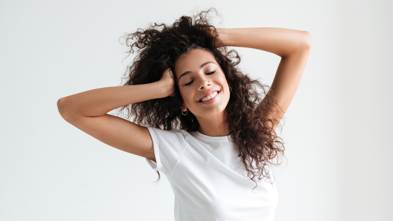 Mulher de cabelo castanho cacheado sorrindo e segurandoi os cabelos