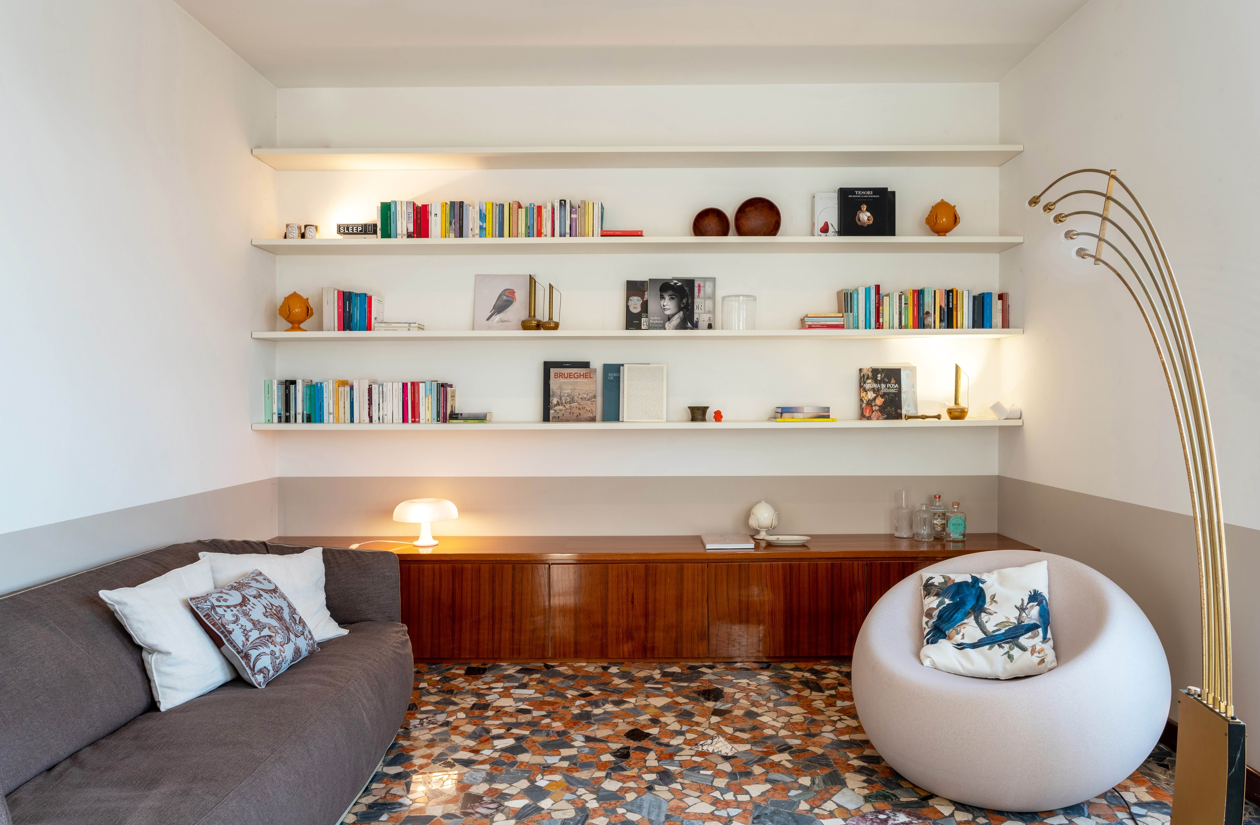 Sala de estar contempor&acirc;nea com paredes brancas, prateleira de livros e piso de caquinho colorido