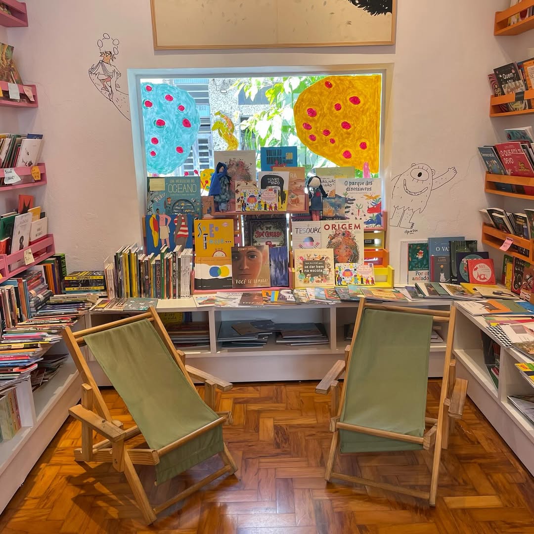 Espa&ccedil;o interno da Livraria Mi&uacute;da com estantes baixas, livros infantis expostos e ambiente l&uacute;dico.