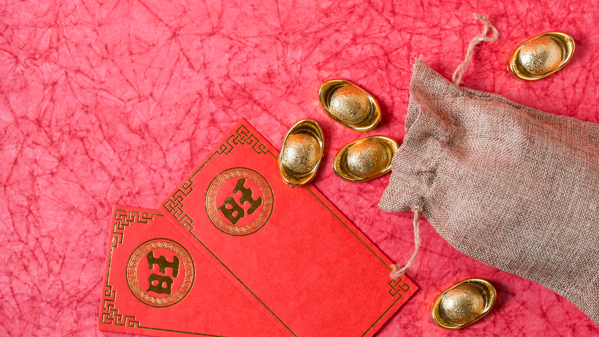 Envelopes vermelhos e moedas douradas aparecem ao lado de um pequeno saco de moedas, símbolos tradicionais de prosperidade na cultura chinesa