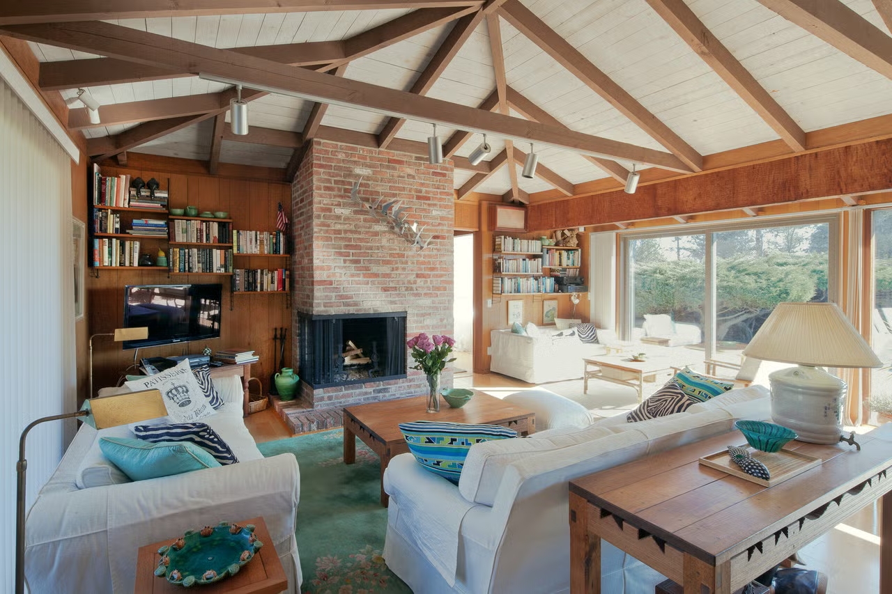 Sala da casa de ver&atilde;o nos Hamptons com lareira de tijolos e vigas aparentes