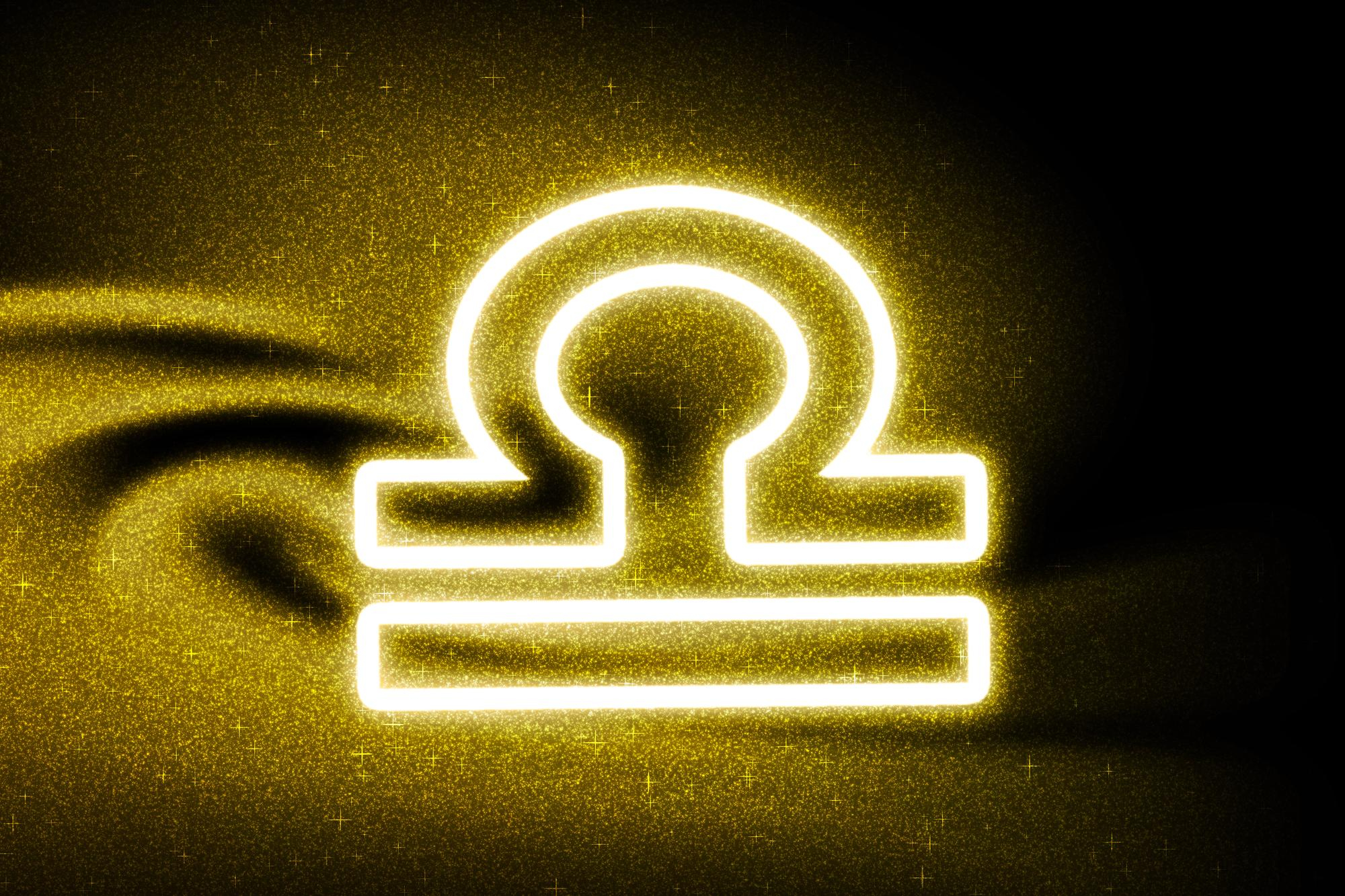 Imagem do símbolo do sígno de libra em fundo preto rodeado de glitter dourado