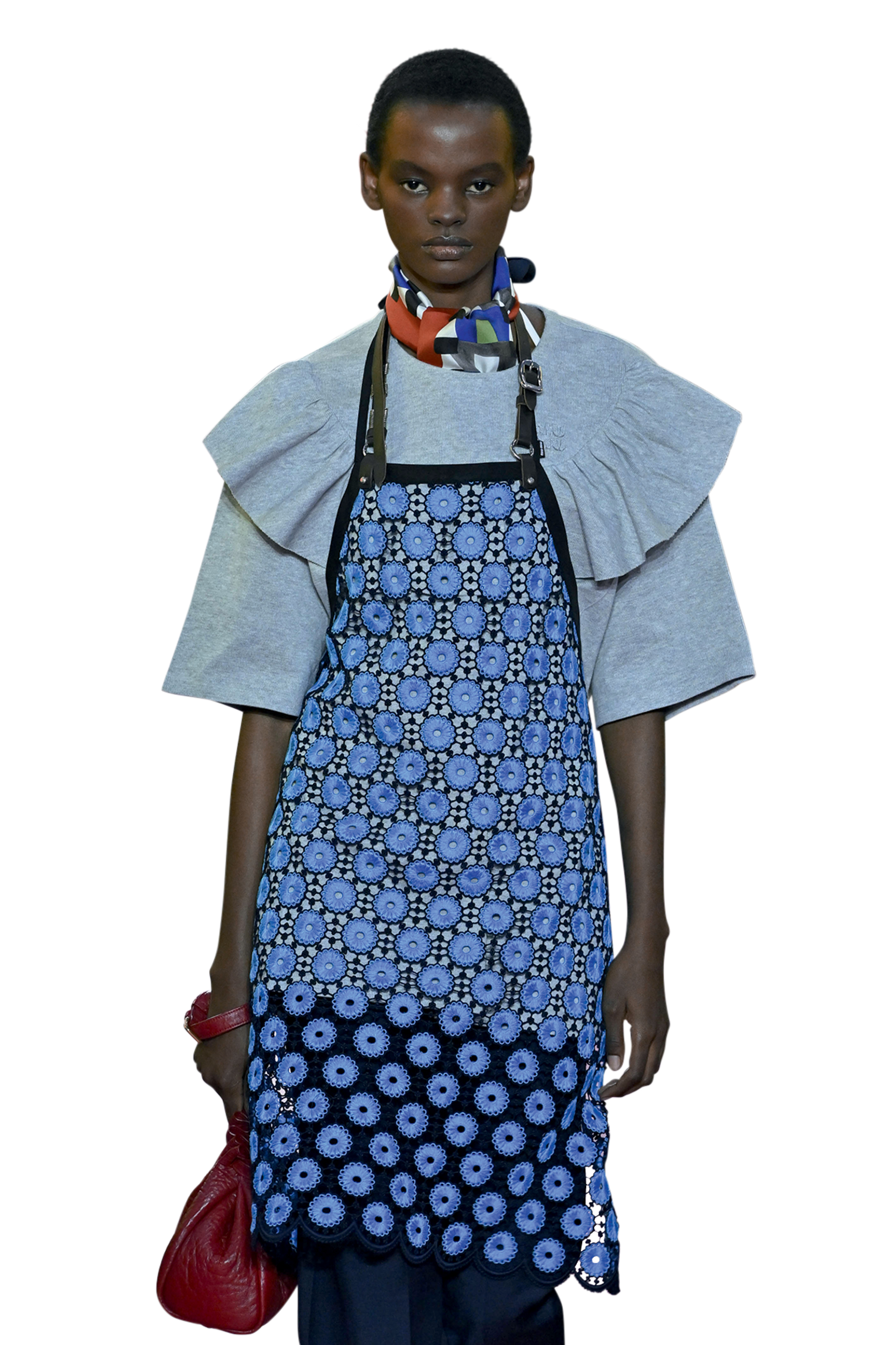 Uma modelo desfila com um look contempor&acirc;neo composto por vestido estampado azul, blusa estruturada e len&ccedil;o colorido no pesco&ccedil;o. O visual representa o di&aacute;logo atual entre moda e narrativa visual.