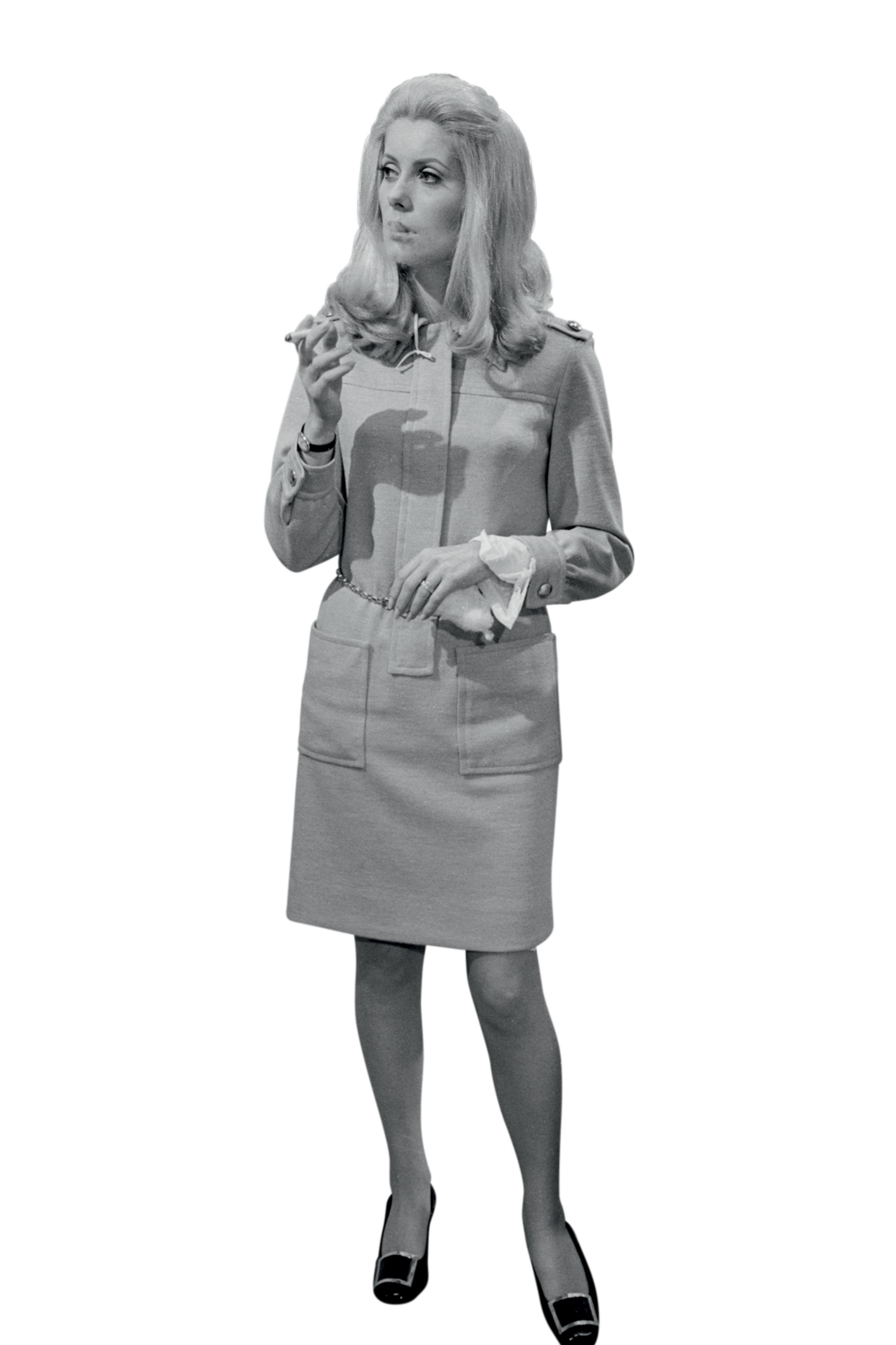 Catherine Deneuve aparece em uma fotografia cl&aacute;ssica em preto e branco, vestindo um conjunto elegante e minimalista enquanto segura um cigarro. A imagem refor&ccedil;a o estilo sofisticado e discreto que marcou sua parceria com Yves Saint Laurent.