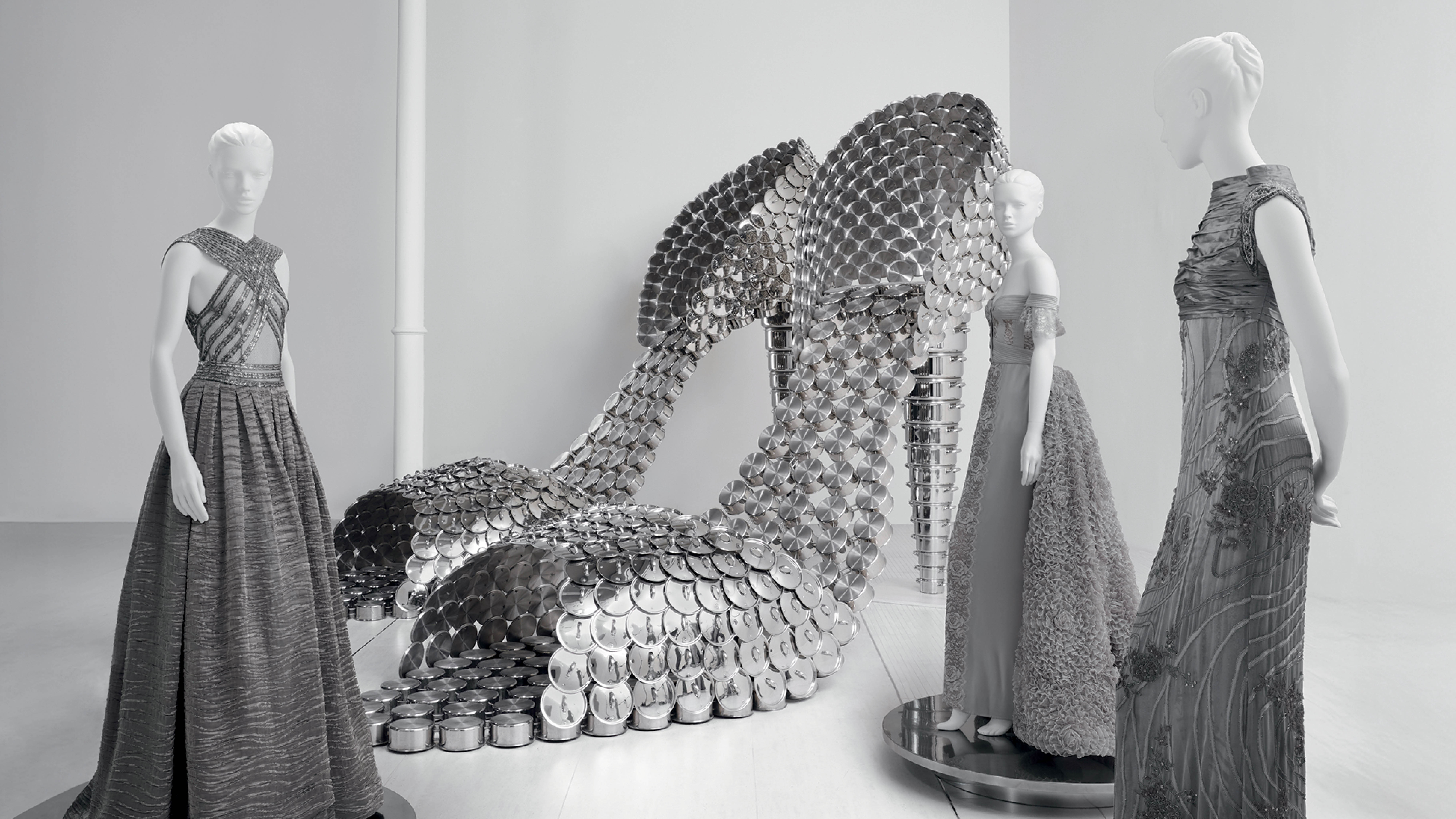 Instalação de moda contemporânea com vestidos metálicos e esculturas em ambiente minimalista, destacando a fusão entre arte, design e alta-costura em exposições atuais