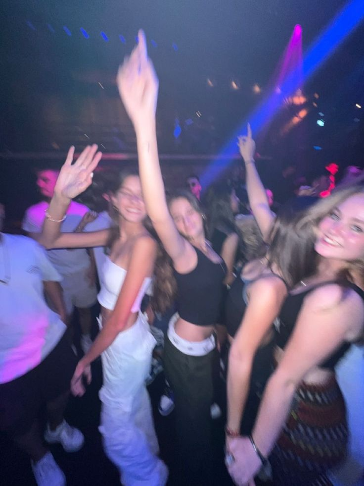 Grupo de amigos dançando em festa com luzes coloridas, criando efeito borrado e movimento na imagem.