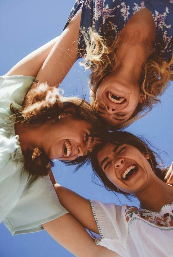 Amigos formando um círculo e olhando para a câmera posicionada abaixo, sorrindo e rindo sob o céu azul.
