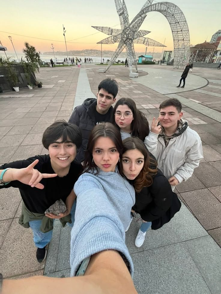 Grupo de amigos posando juntos ao ar livre, com uma pessoa em primeiro plano tirando selfie e os demais ao fundo.