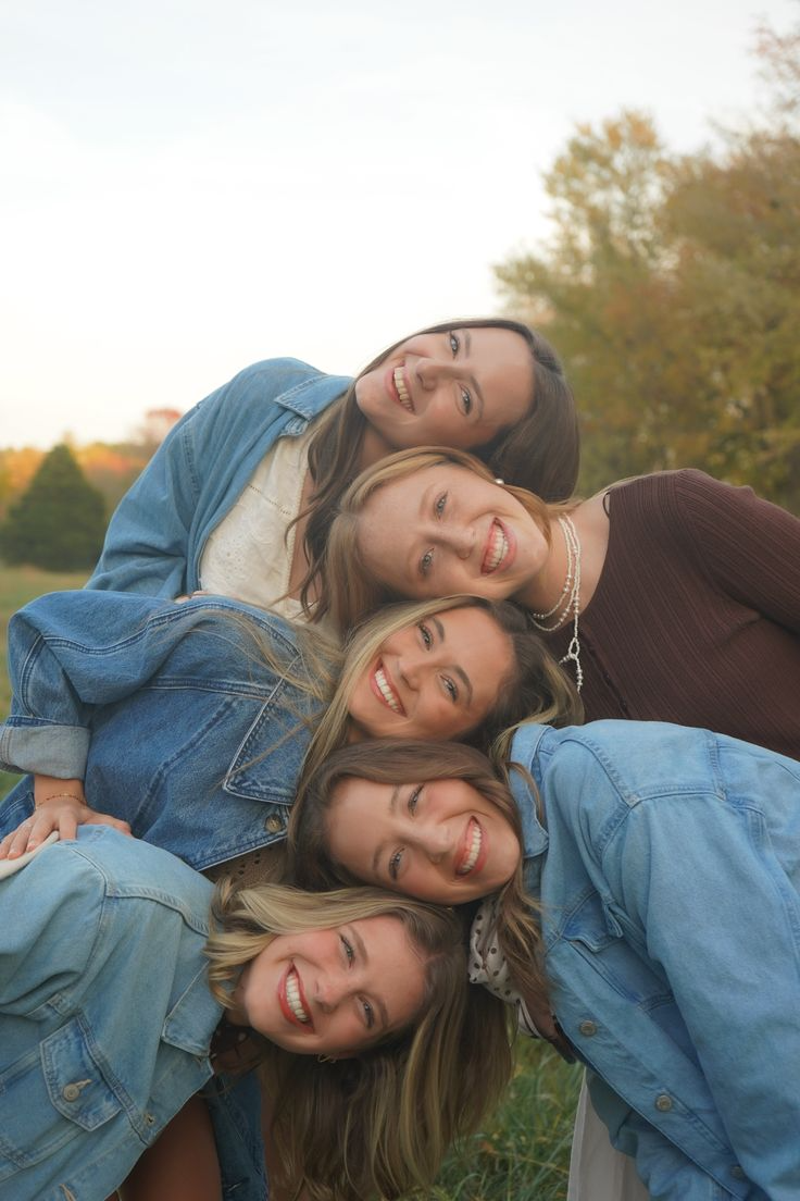 Amigas posando empilhadas, apoiando a cabeça umas nas outras, sorrindo em ambiente externo.