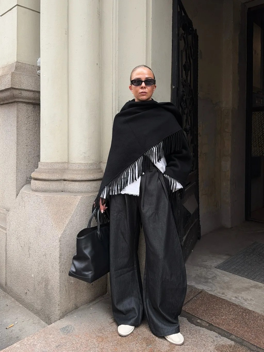 Foto de uma mulher morena usando um look composto por camisa branca, calça, bolsa preta e óculos de sol