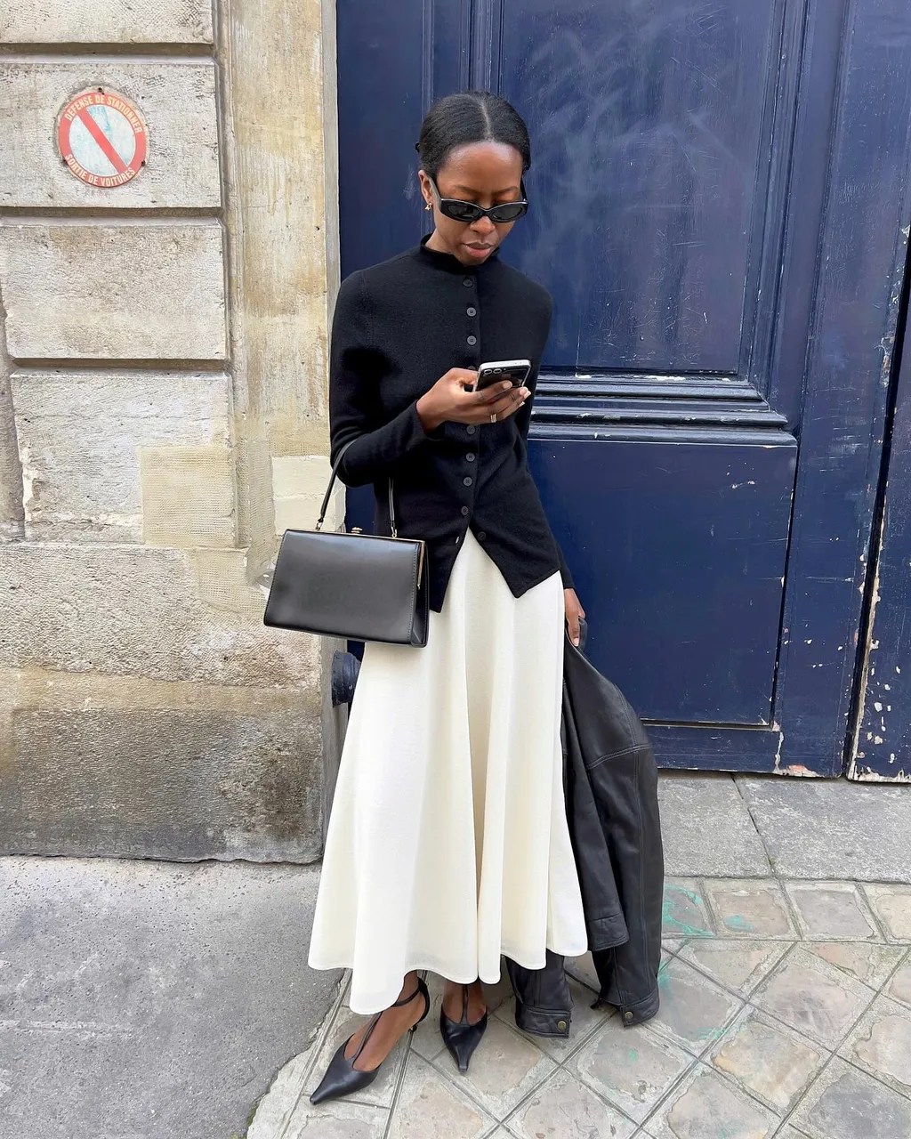Foto de uma mulher negra usanado um look composto por blusa preta, saia branca e salto