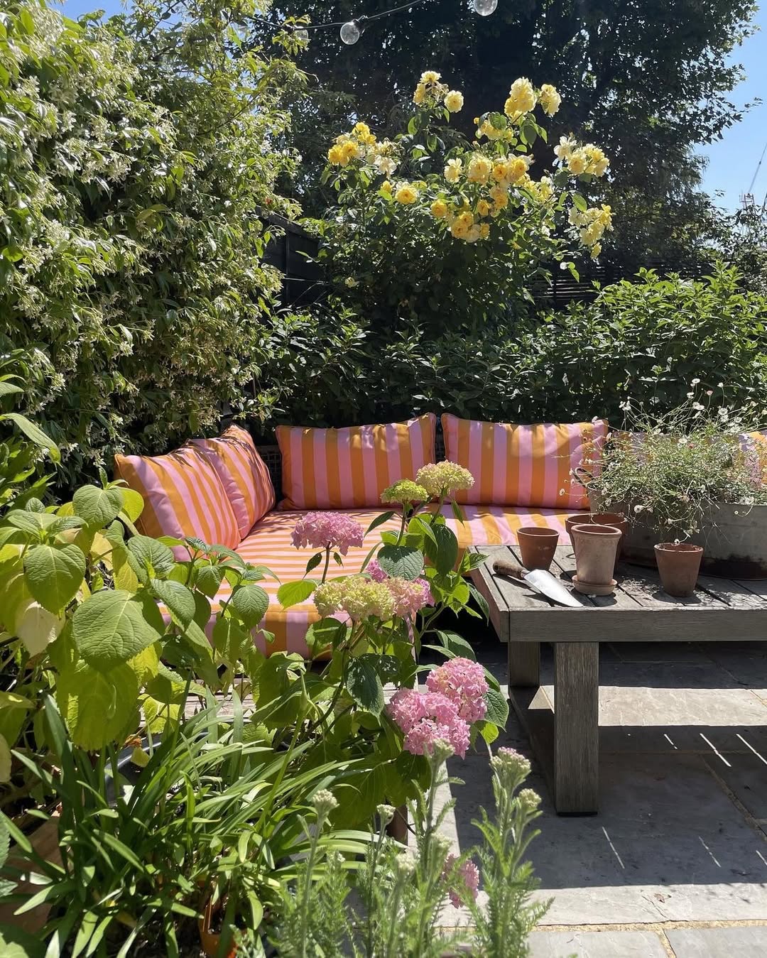 Quintal com jardim campestre e sof&aacute; listrado vermelho e rosa