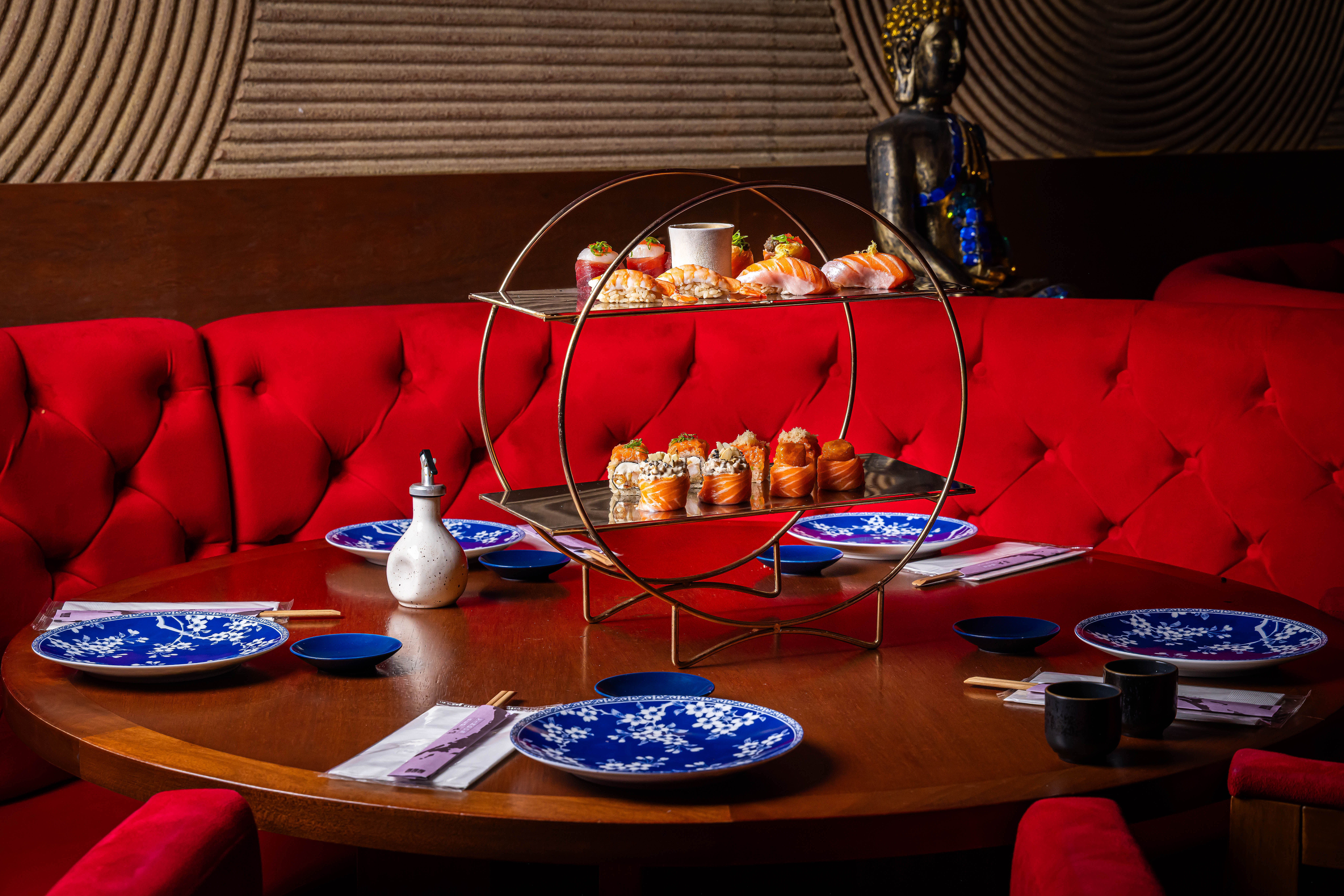 Comida japonesa servida em mesa com sof&aacute; vermelho em volta