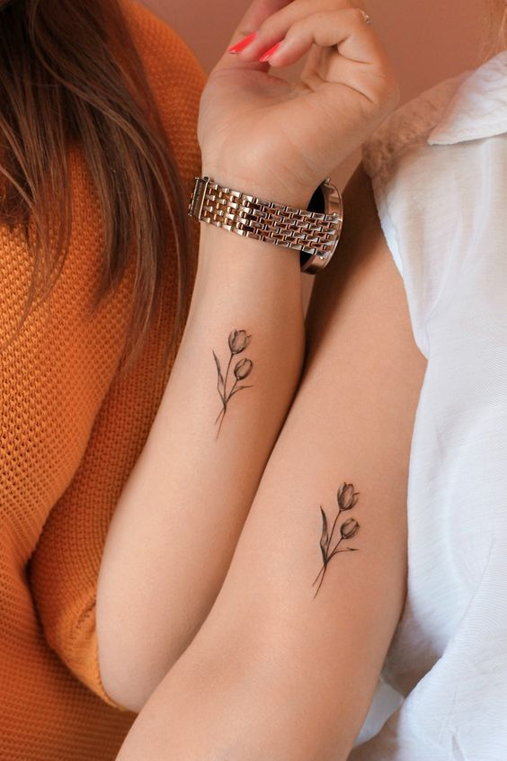 Duas mulheres com tatuagens delicadas de flores iguais nos braços