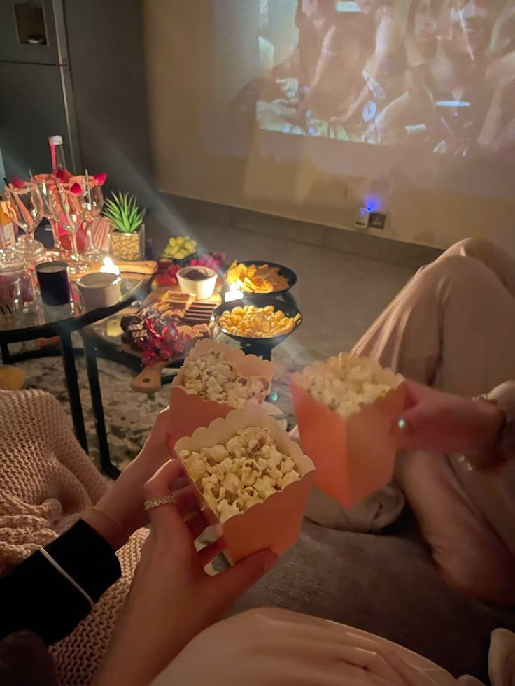 Duas pessoas brindando com pipoca durante noite de filmes em casa.