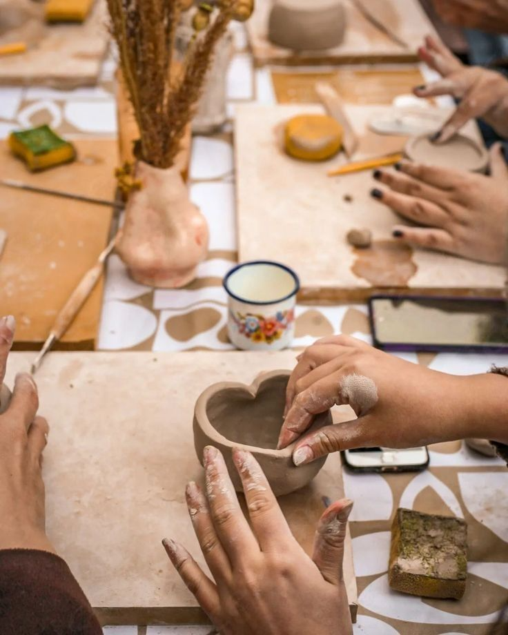 Mãos moldando um recipiente de cerâmica em formato de coração durante aula artesanal.