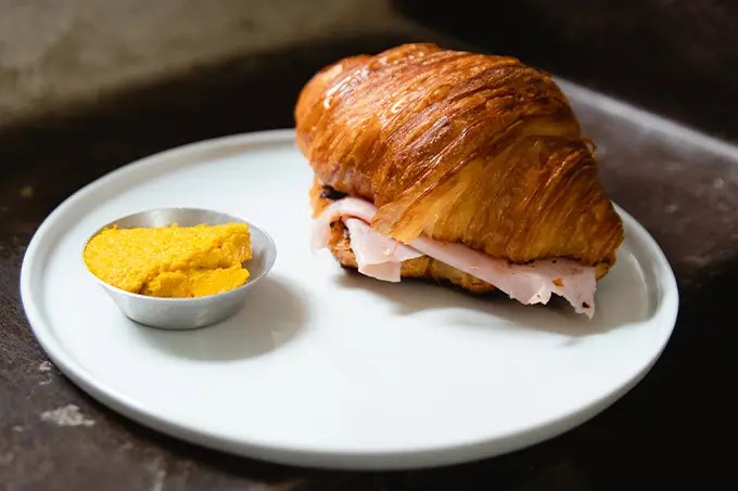 Croissant recheado servido em prato branco ao lado de molho amarelo