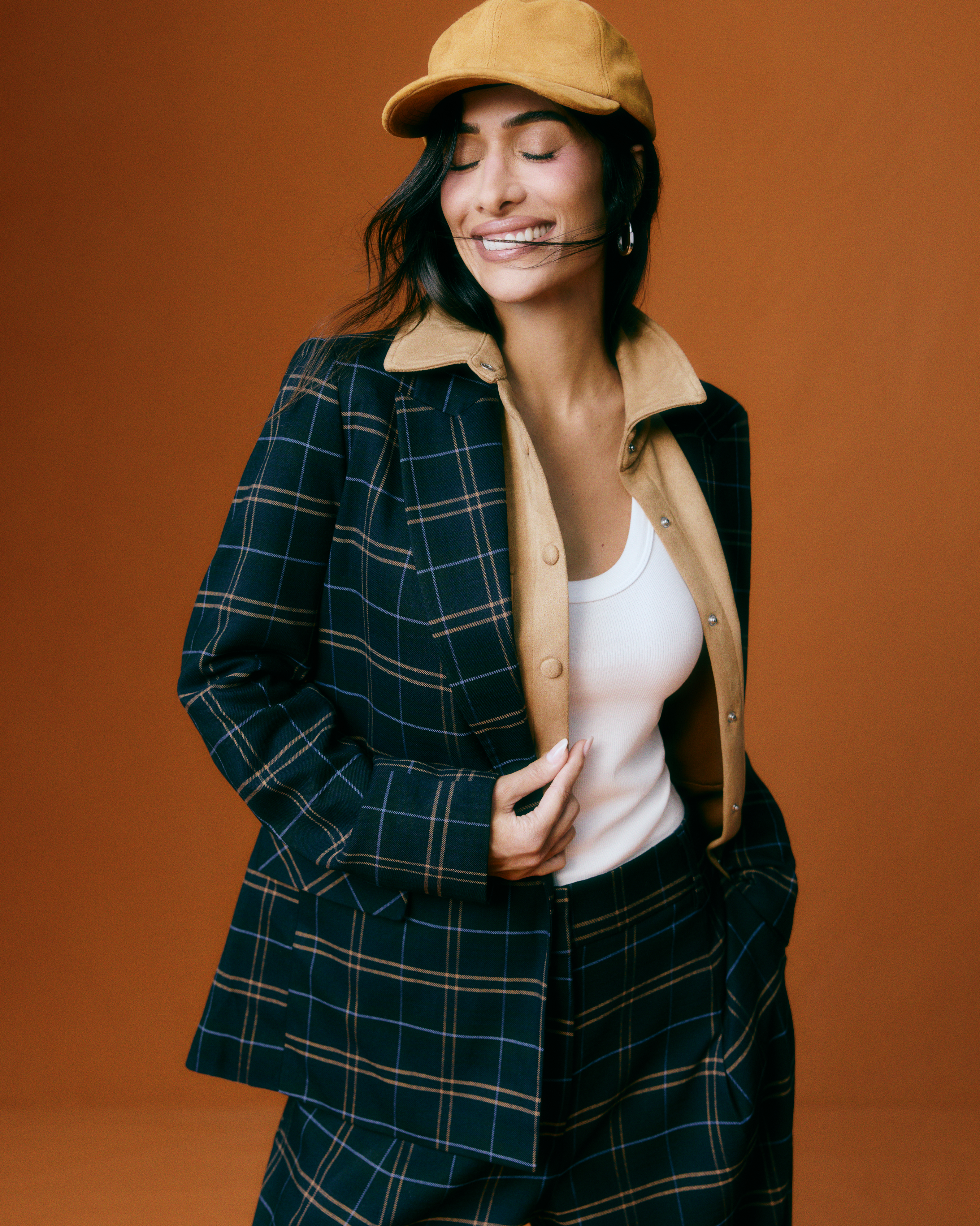 Silvia Braz em look elegante com blazer xadrez, camisa bege e bon&eacute;, representando a moda atemporal e vers&aacute;til da cole&ccedil;&atilde;o em parceria com a Riachuelo