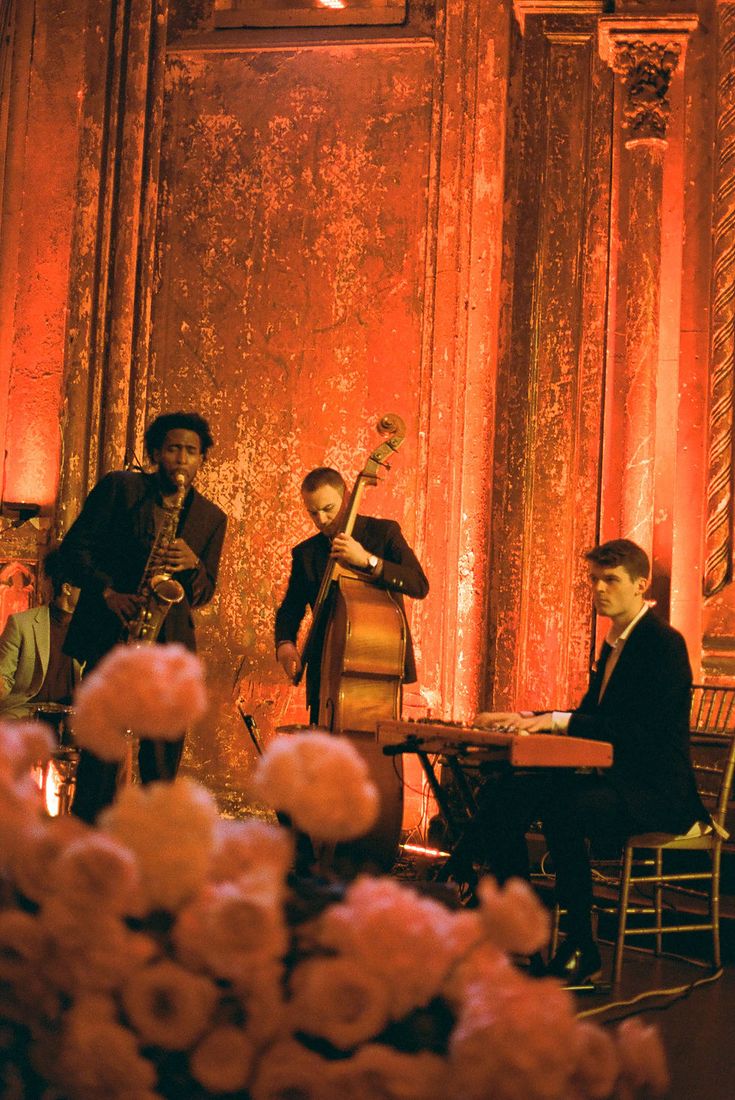 Banda de jazz ao vivo com saxofonista, contrabaixista e tecladista em sal&atilde;o com paredes envelhecidas