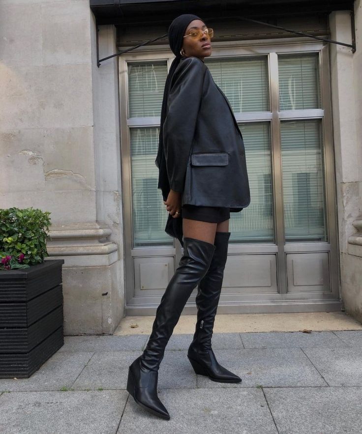 Mulher usa blazer preto oversized, shorts e botas pretas over the knee de salto alto em um look sofisticado e moderno. O modelo de cano super longo aparece como uma das apostas mais elegantes e sensuais para os dias frios.