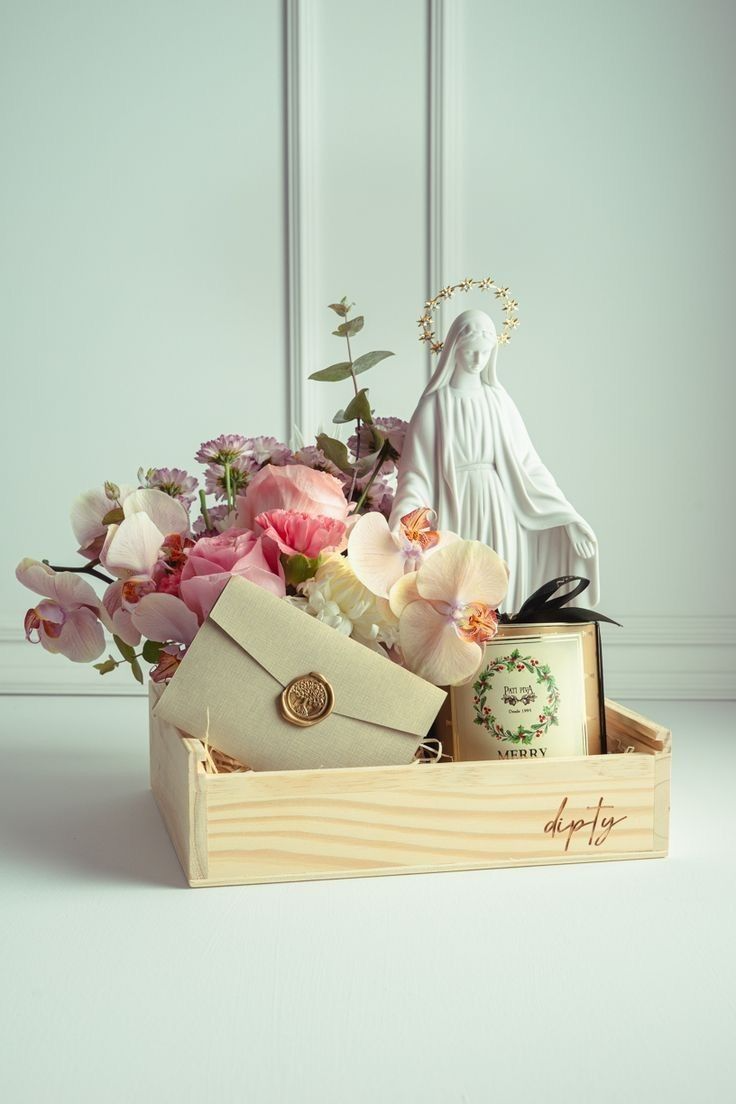 Cesta com imagem religiosa, flores delicadas, vela e envelope decorativo em composição suave e elegante.