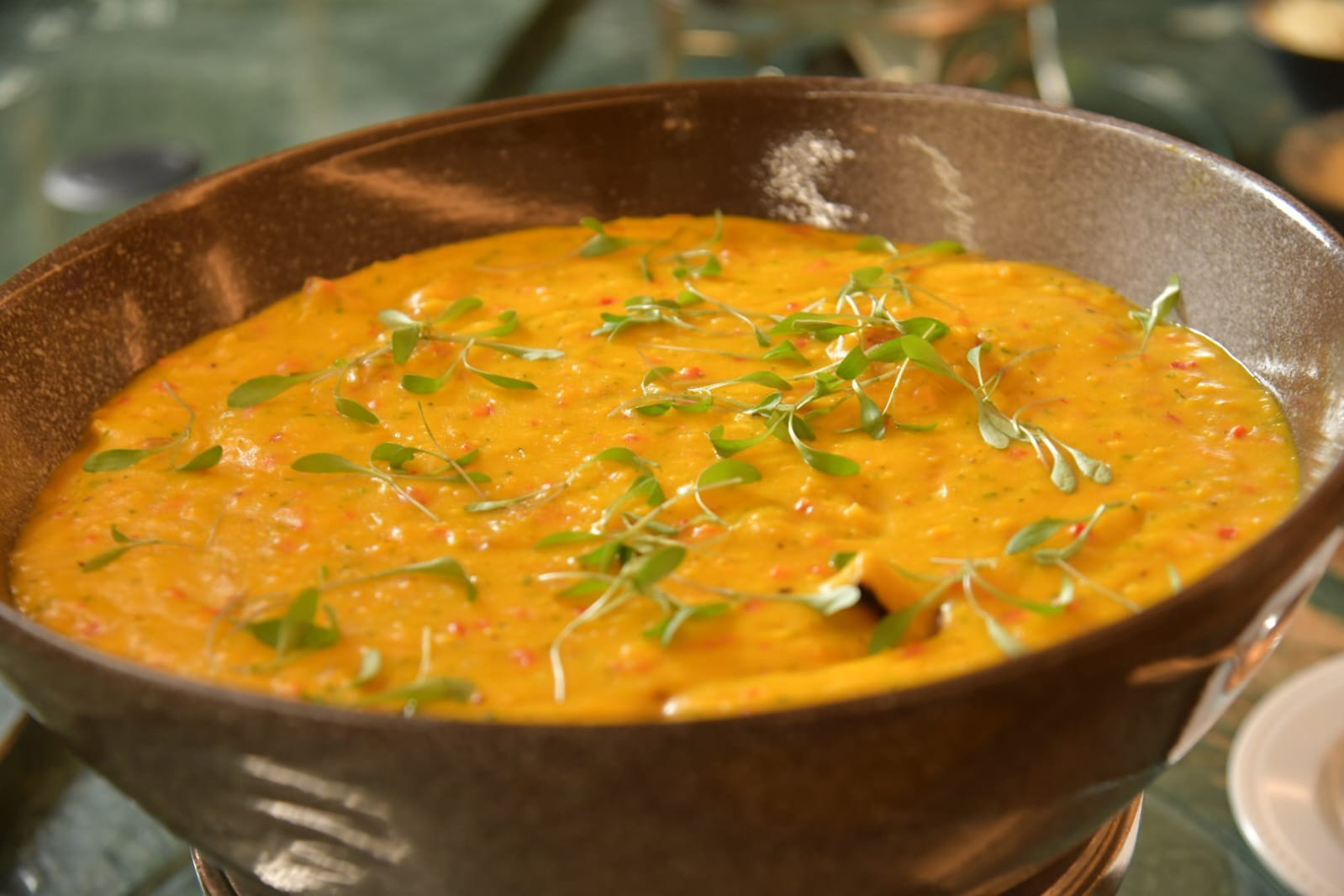 Creme de ab&oacute;bora ou mandioquinha em tigela r&uacute;stica marrom, decorado com folhas verdes de microgreens e pedacinhos vermelhos de piment&atilde;o ou pimenta