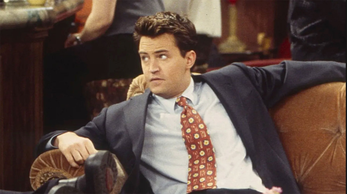 Cena de Friends mostra Chandler Bing sentado no sof&aacute; usando terno e gravata