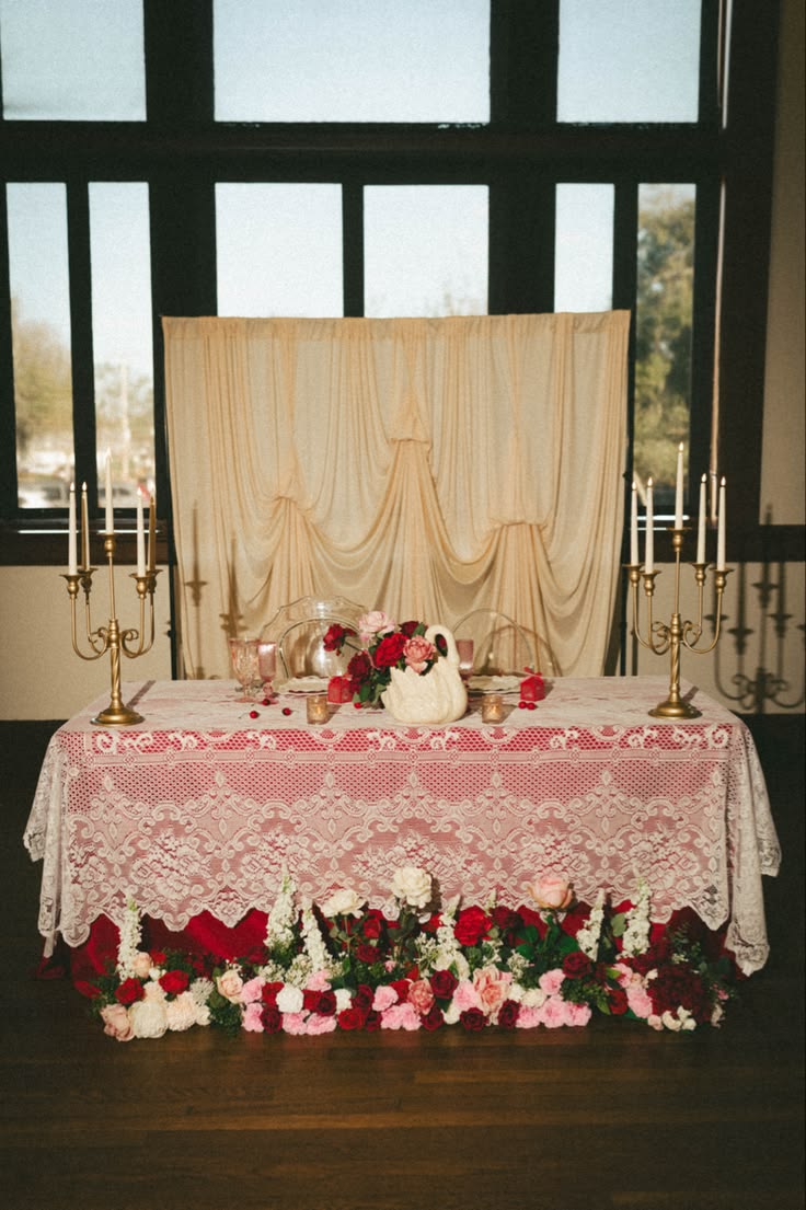 Mesa do casal com toalha de renda, casti&ccedil;ais dourados, arranjo de rosas e jarra de cisne em porcelana