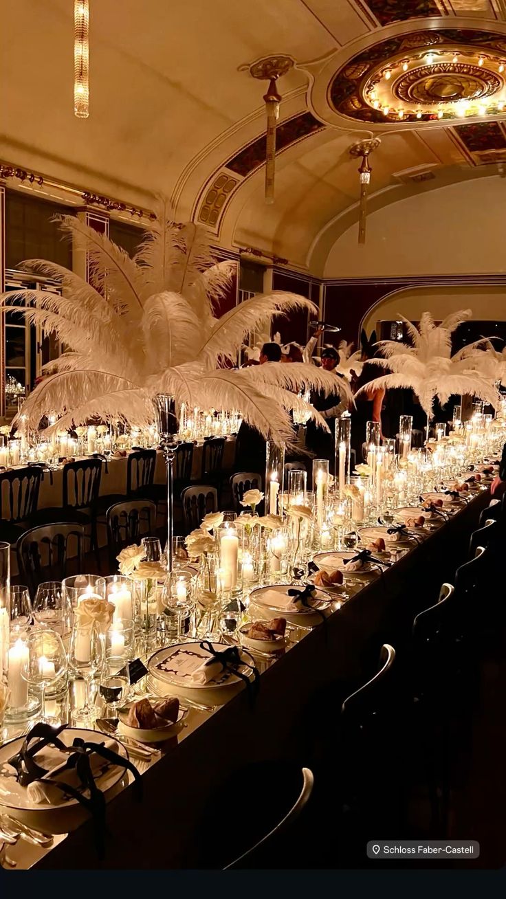 Mesa longa com arranjos de plumas de avestruz brancas em casti&ccedil;ais de cristal