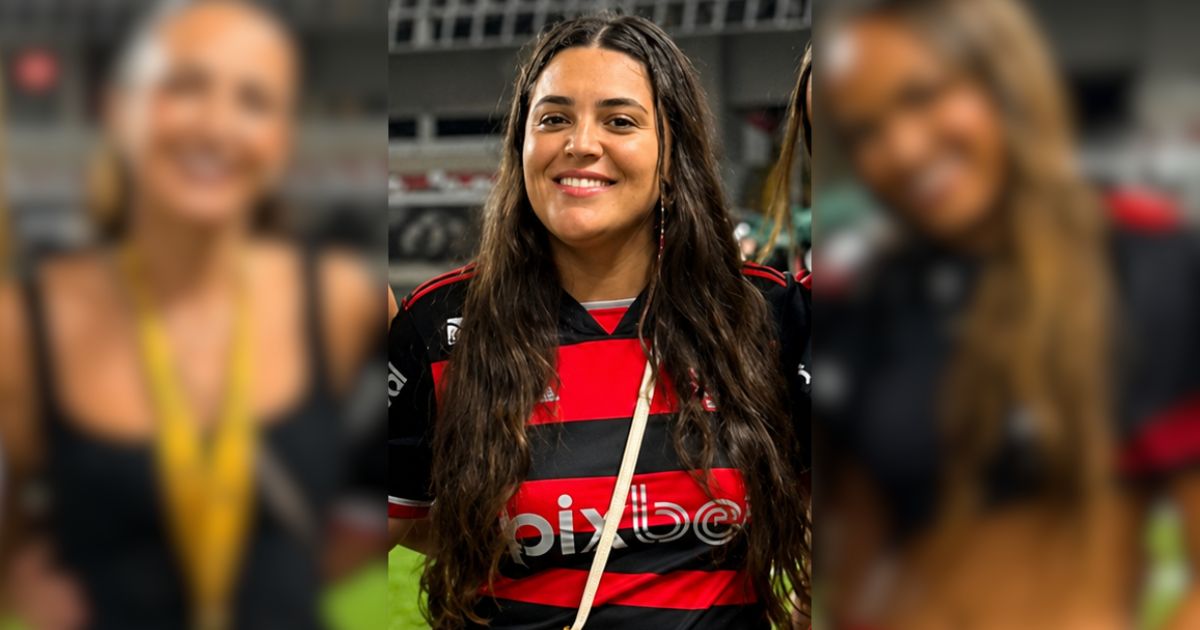 Mulher de cabelos longos e castanhos, sorrindo, vestindo camisa preta e vermelha do Flamengo com o logo 