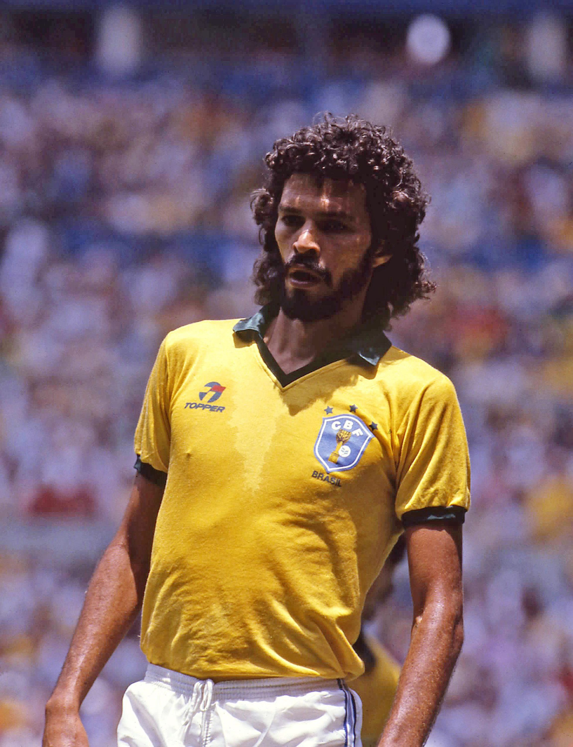Falc&atilde;o, jogador de futebol, em campo com a camisa amarela da sele&ccedil;&atilde;o brasileira, gola e mangas verdes, suado, cabelo e barba castanhos encaracolados, olhando para a direita com express&atilde;o s&eacute;ria