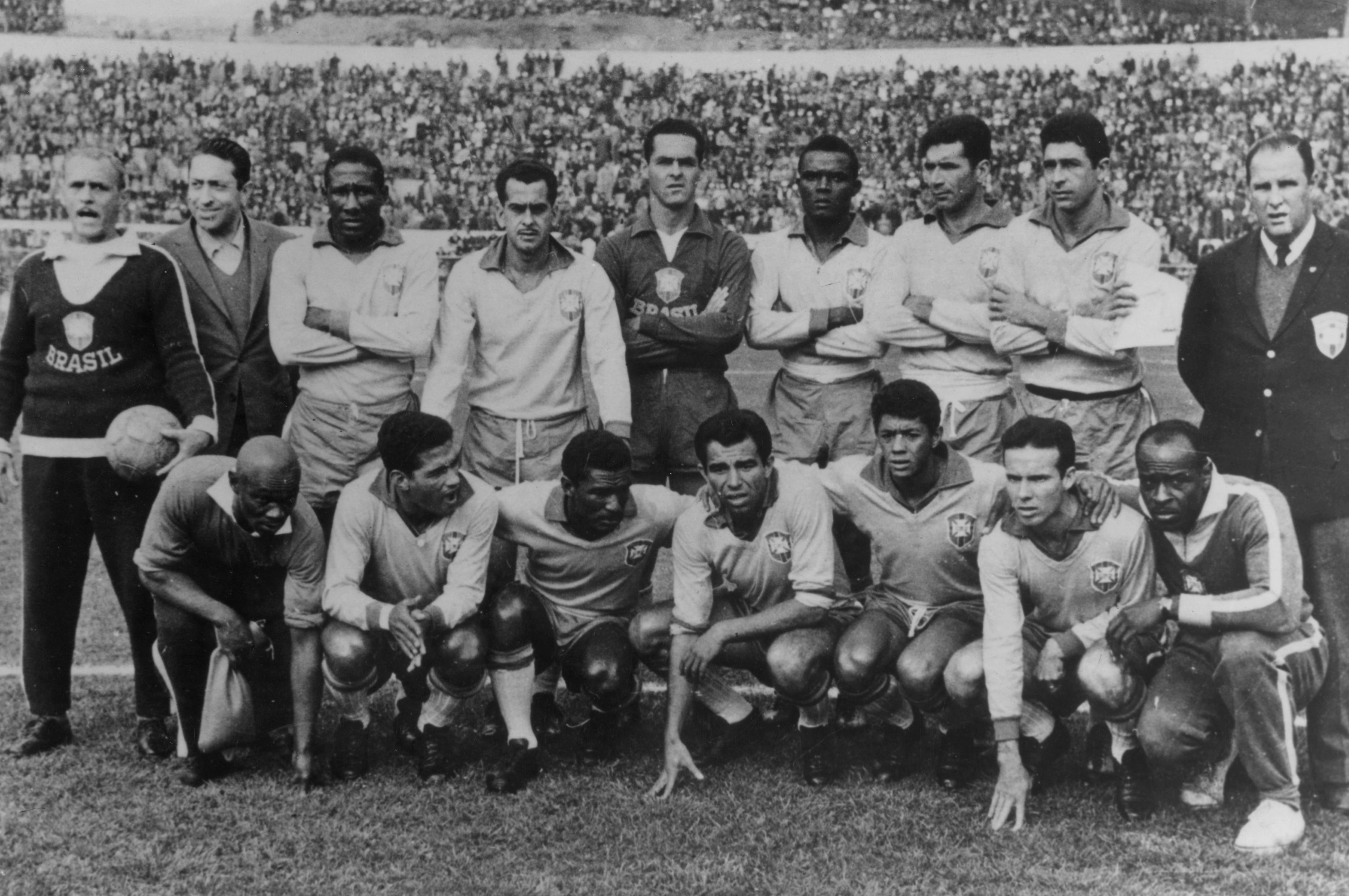 Time de futebol brasileiro posa para foto em campo, com 11 jogadores de camisa clara e shorts escuros, sendo 6 em p&eacute; e 5 agachados, e 3 homens de terno, um deles segurando uma bola. A arquibancada lotada aparece ao fundo