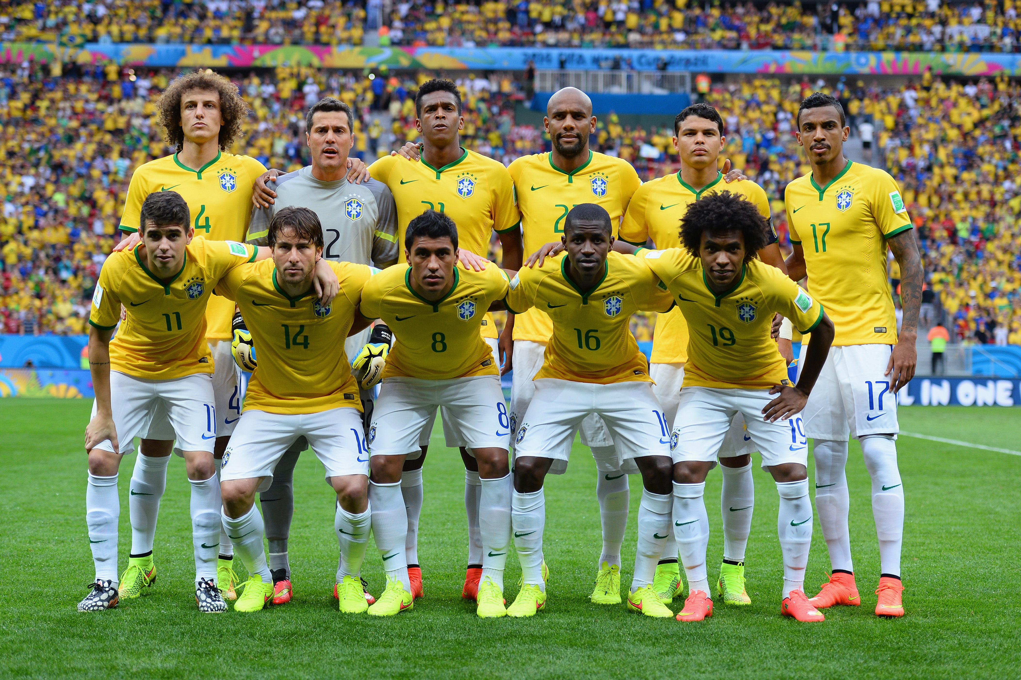 Jogadores da sele&ccedil;&atilde;o brasileira de futebol posam para foto em campo, vestindo camisas amarelas e cal&ccedil;&otilde;es brancos, com a torcida ao fundo