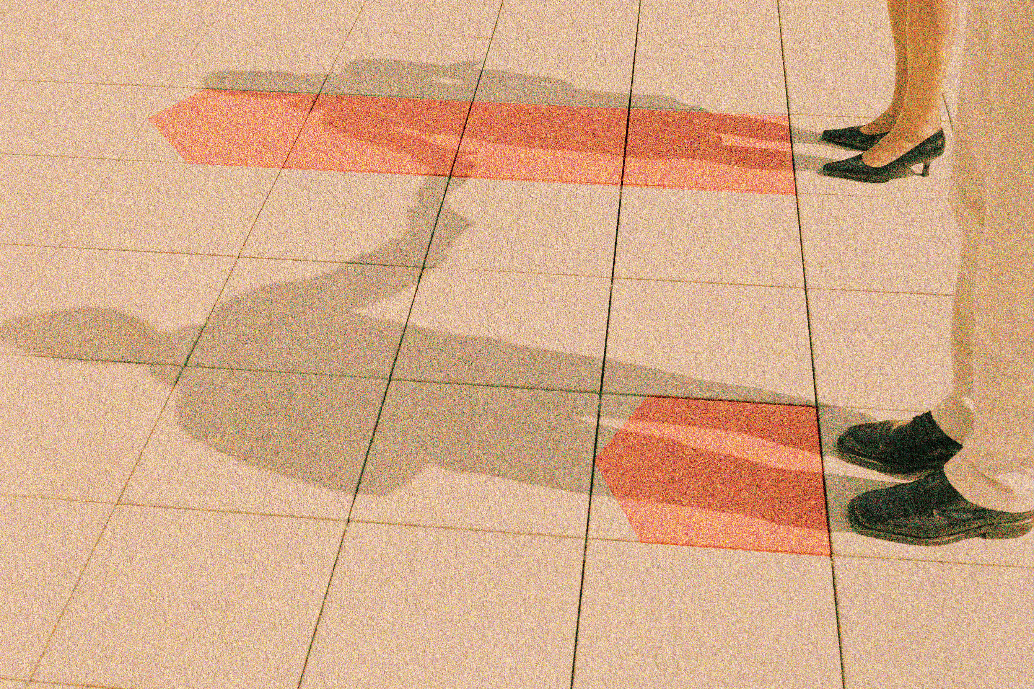 P&eacute;s de duas pessoas em um piso de ladrilhos claros, com suas sombras projetadas e duas setas vermelhas pintadas no ch&atilde;o, indicando dire&ccedil;&otilde;es opostas