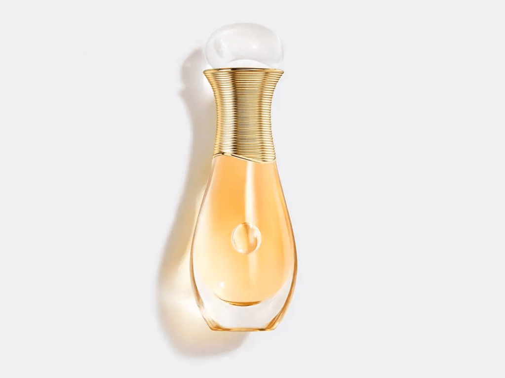 Frasco de perfume Jadore da Dior, com l&iacute;quido dourado, corpo de vidro transparente em formato de gota e gargalo dourado com an&eacute;is, tampa esf&eacute;rica transl&uacute;cida. Fundo branco