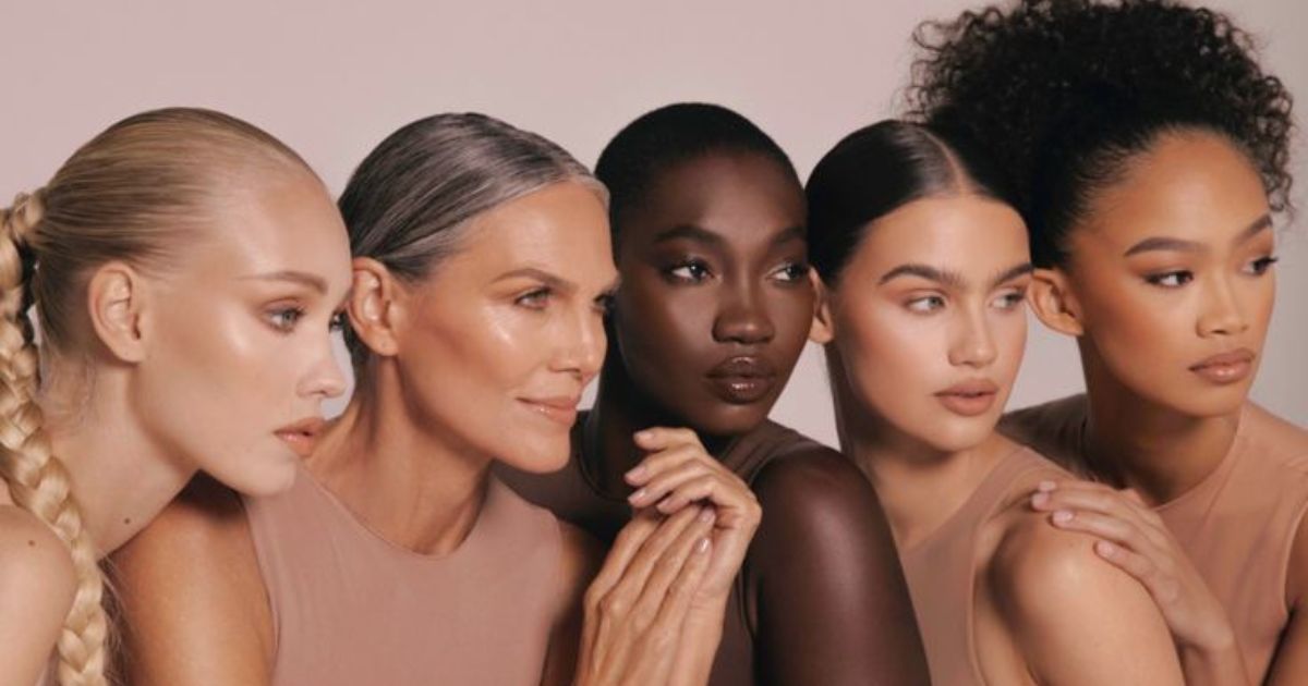 Cinco mulheres de diferentes etnias e idades, com maquiagem natural e tons de pele variados, posam juntas em um fundo claro, representando diversidade e beleza