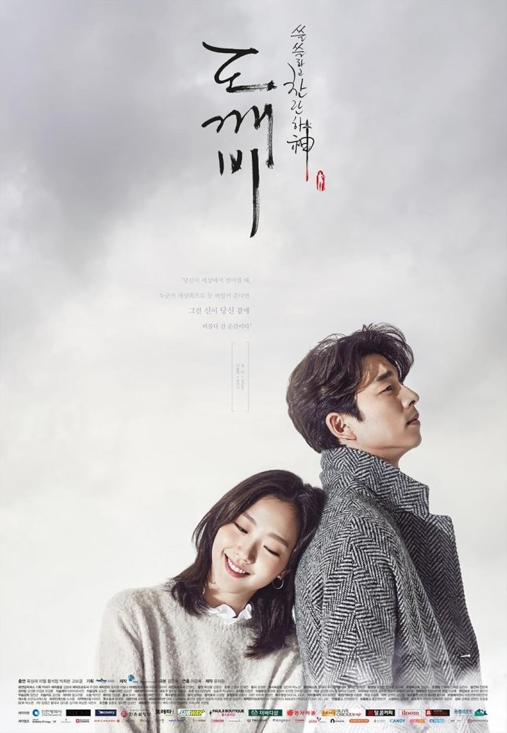 P&ocirc;ster de Goblin com um homem e uma mulher. Ele, de perfil, olha para cima, usando casaco cinza. Ela, sorrindo com olhos fechados, apoia a cabe&ccedil;a nas costas dele, vestindo su&eacute;ter creme. O t&iacute;tulo em coreano est&aacute; no topo, com texto e logos de patrocinadores na parte inferior. O fundo &eacute; um c&eacute;u nublado
