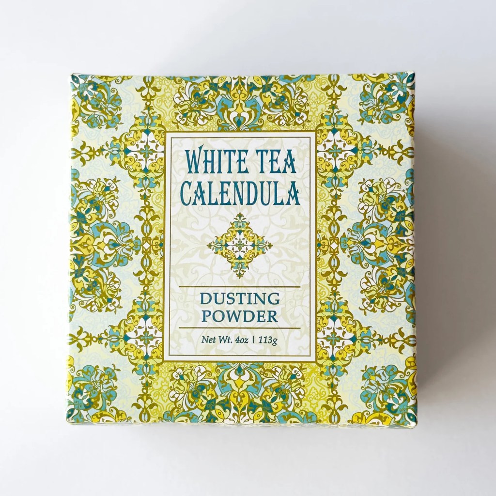 Caixa quadrada de p&oacute; de ch&aacute; branco e cal&ecirc;ndula, com estampa floral em tons de verde-lim&atilde;o, azul-petr&oacute;leo e amarelo. No centro, um r&oacute;tulo creme com WHITE TEA CALENDULA DUSTING POWDER e Net Wt. 4oz | 113g