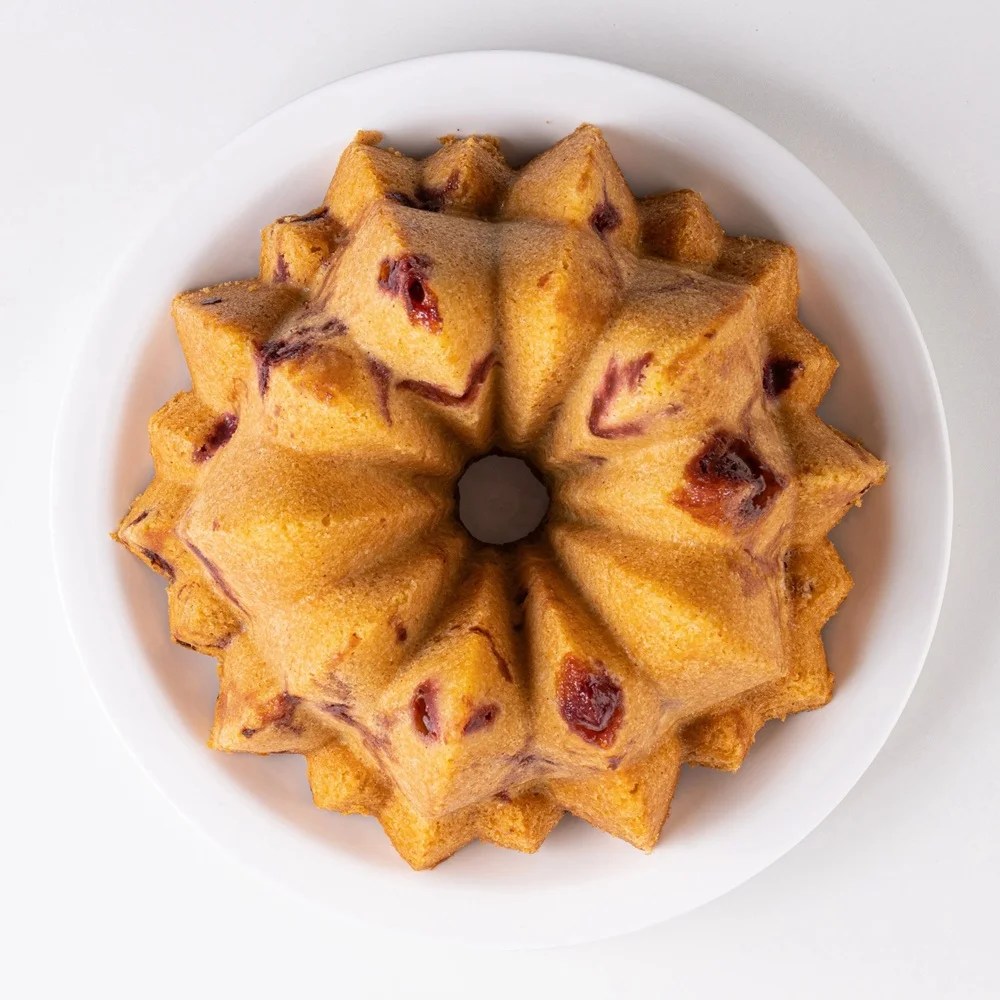 Bolo caseiro em formato de estrela, com massa dourada e peda&ccedil;os de frutas vermelhas vis&iacute;veis, servido em um prato branco sobre fundo claro
