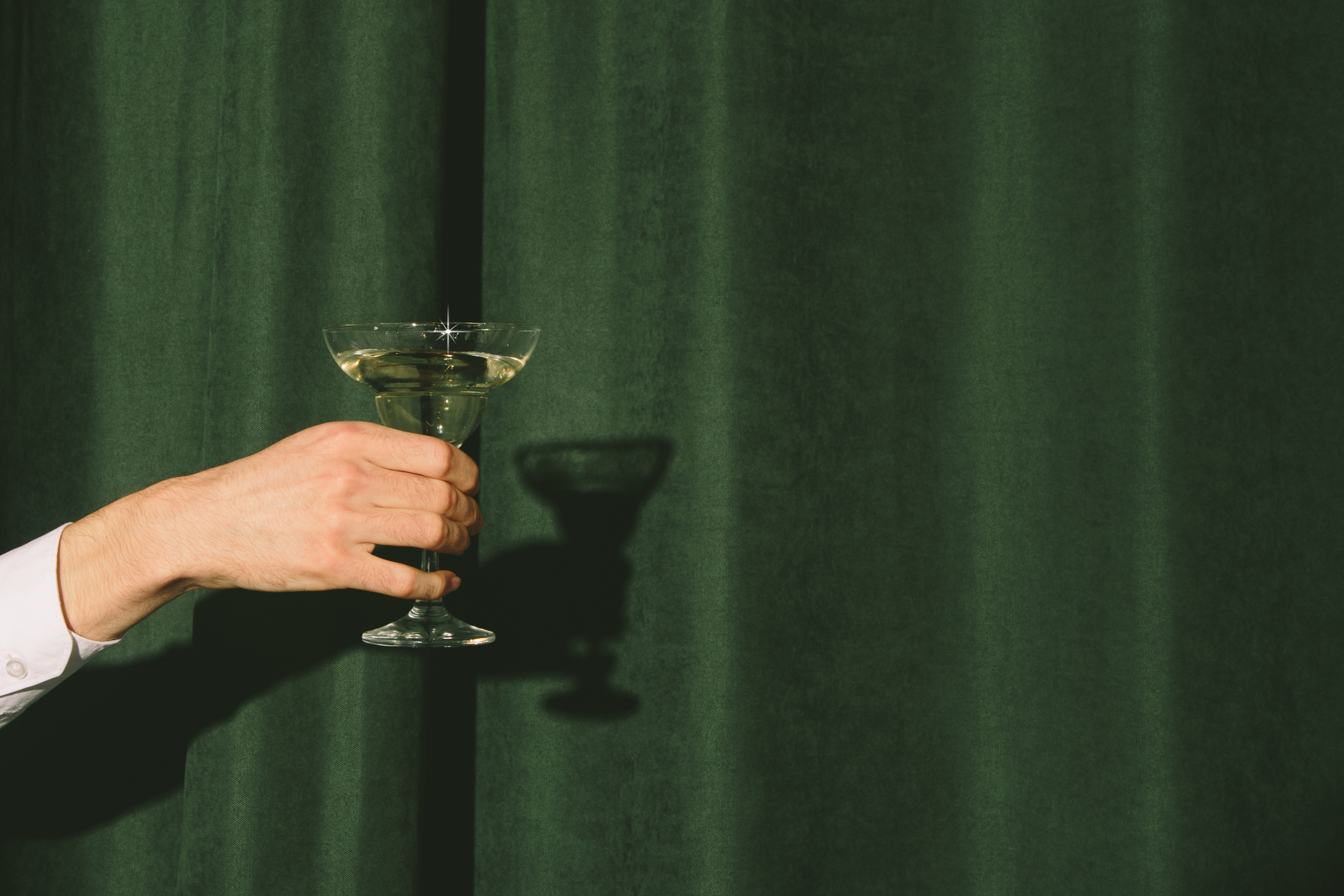 Hand with a martini glass sticks out from the curtains