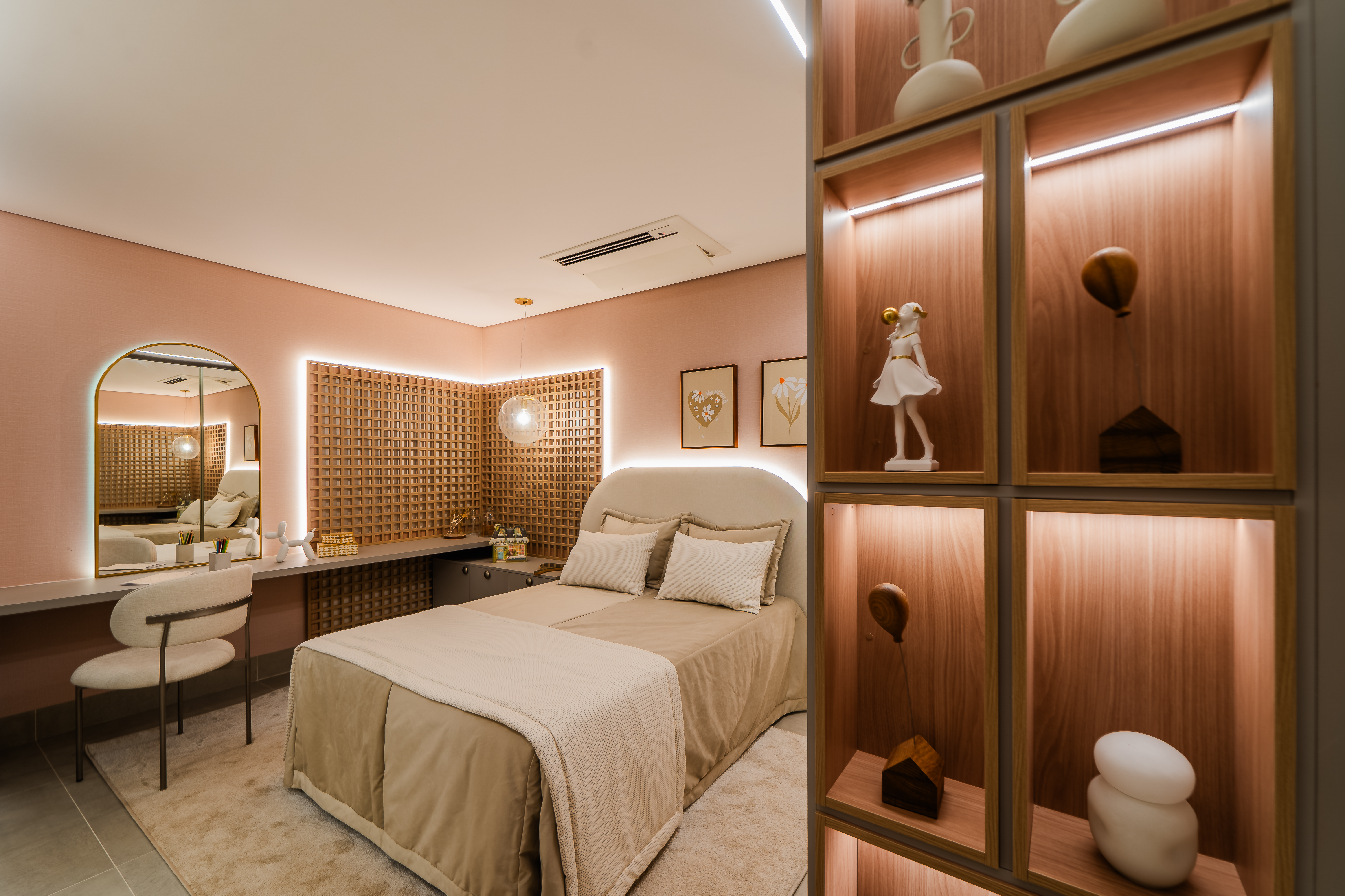 Quarto moderno com paredes rosa claro, cama de casal bege, espelho arqueado, penteadeira com cadeira branca e prateleiras de madeira iluminadas com objetos decorativos