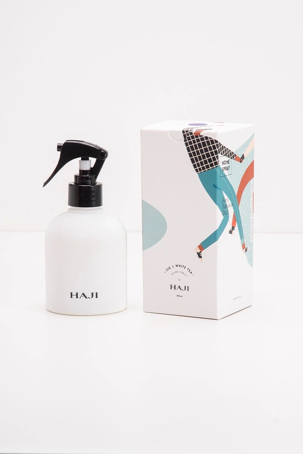 Frasco branco de spray para ambientes da marca HAJI com bico preto, ao lado de uma caixa branca com ilustra&ccedil;&atilde;o colorida e a descri&ccedil;&atilde;o Fig & White Tea Home Spray