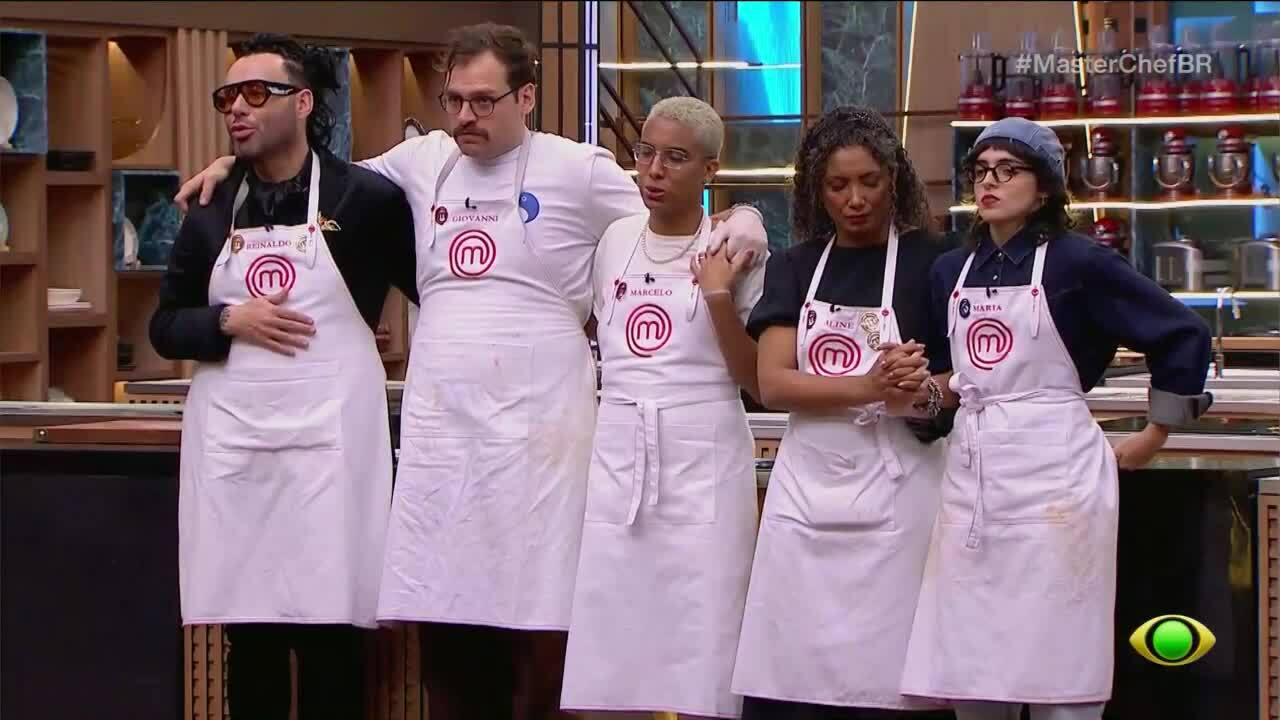 Cinco participantes do MasterChef Brasil, tr&ecirc;s homens e duas mulheres, vestem aventais brancos com o logo vermelho do programa e seus nomes. Eles est&atilde;o lado a lado, com express&otilde;es s&eacute;rias, em uma cozinha profissional. O homem da esquerda usa &oacute;culos escuros e tem o bra&ccedil;o sobre o ombro do segundo homem, que tem bigode. A mulher do centro tem cabelo curto e loiro, e o bra&ccedil;o sobre o ombro da quarta mulher, de cabelo cacheado. A &uacute;ltima mulher, &agrave; direita, usa um gorro azul e &oacute;culos. Ao fundo, prateleiras com utens&iacute;lios de cozinha e a hashtag #MasterChefBR