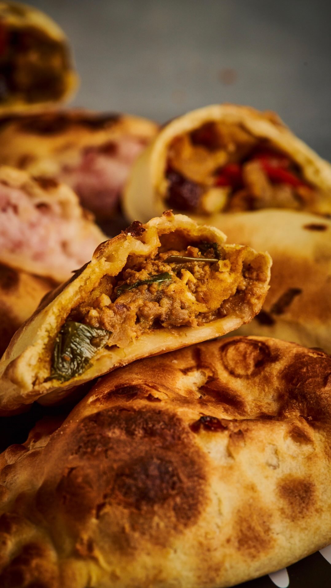 Empanada assada, cortada ao meio, revelando recheio de carne mo&iacute;da, cebola e folhas verdes, sobre outras empanadas douradas