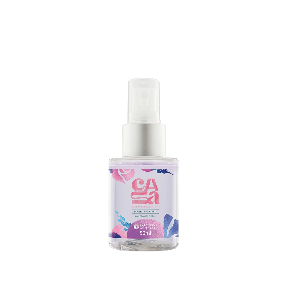 Frasco transparente de spray LOccitane Au Br&eacute;sil, linha Casa Brasileira, 50ml, com l&iacute;quido lil&aacute;s e r&oacute;tulo decorado com flores e folhas em tons de rosa, azul e roxo. O bico &eacute; branco e a tampa prateada