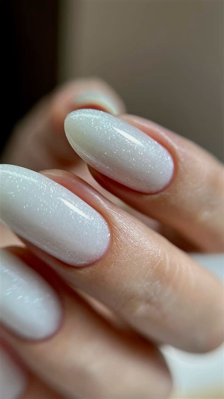 M&atilde;o feminina com unhas ovais longas, esmaltadas em branco perolado com brilho sutil, destacando a cut&iacute;cula bem cuidada