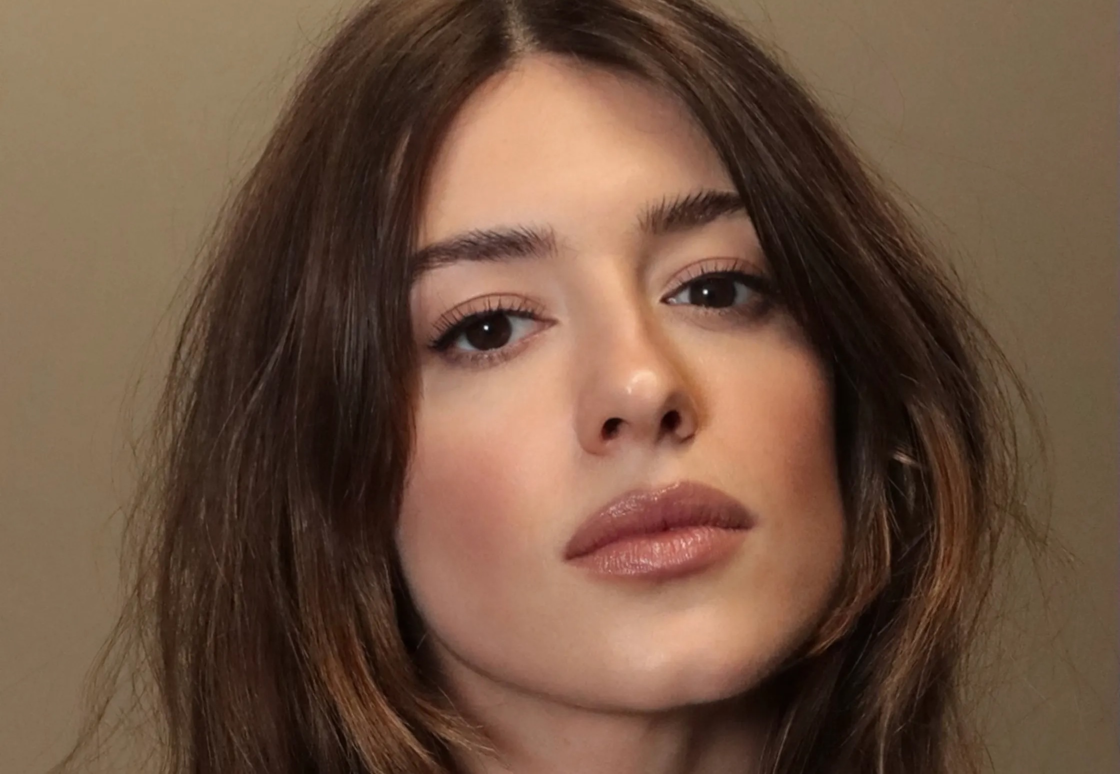 Rosto de uma mulher jovem com cabelo castanho escuro e maquiagem natural, olhando diretamente para a câmera com expressão séria