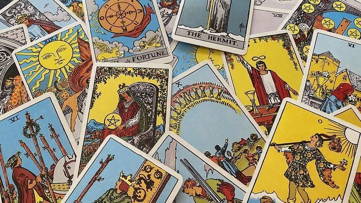 Várias cartas de tarô espalhadas, com ilustrações coloridas de figuras como O Sol, A Roda da Fortuna, O Eremita e A Imperatriz, em tons de amarelo, azul e vermelho