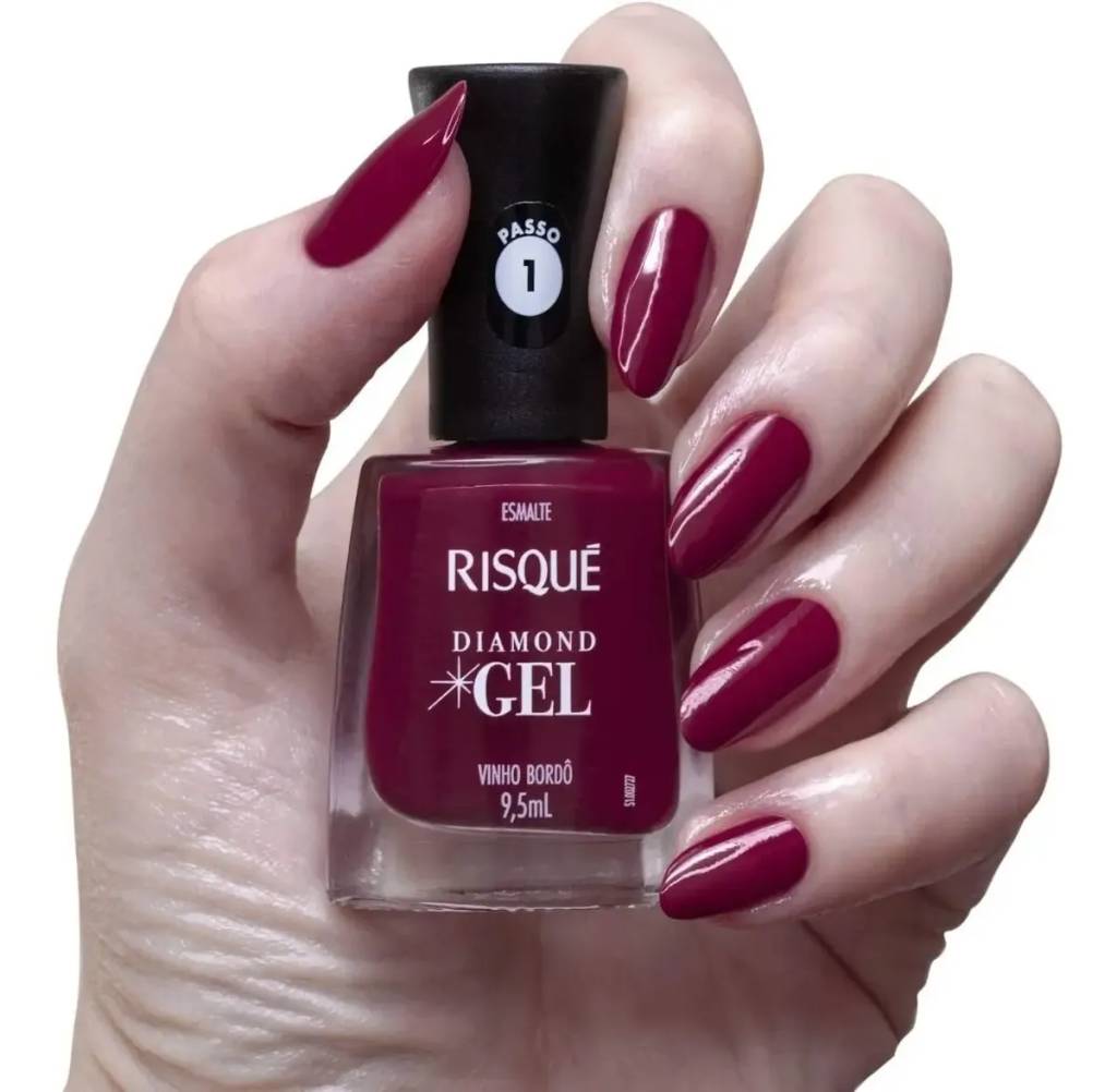 M&atilde;o feminina segurando um esmalte Risqu&eacute; Diamond Gel Vinho Bord&ocirc;, com unhas pintadas na mesma cor, brilhantes e bem cuidadas